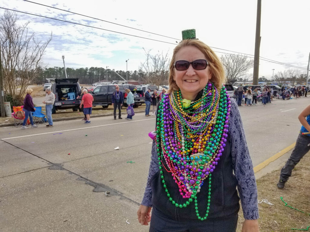 Connie standing on parade route wearing a tiny green tophat and a LOT of beads around her neck.
