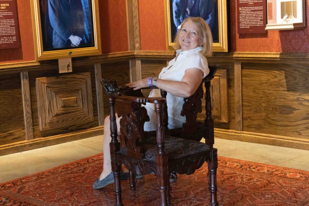 Connie sitting on a chair in front of holograms in the new section of the Boot Hill Museum