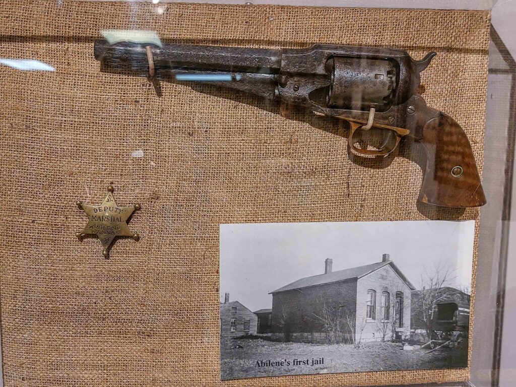 Gun and an Abilene Deputy Marshal star-shaped badge. Also a photo of Abilene's first jail.