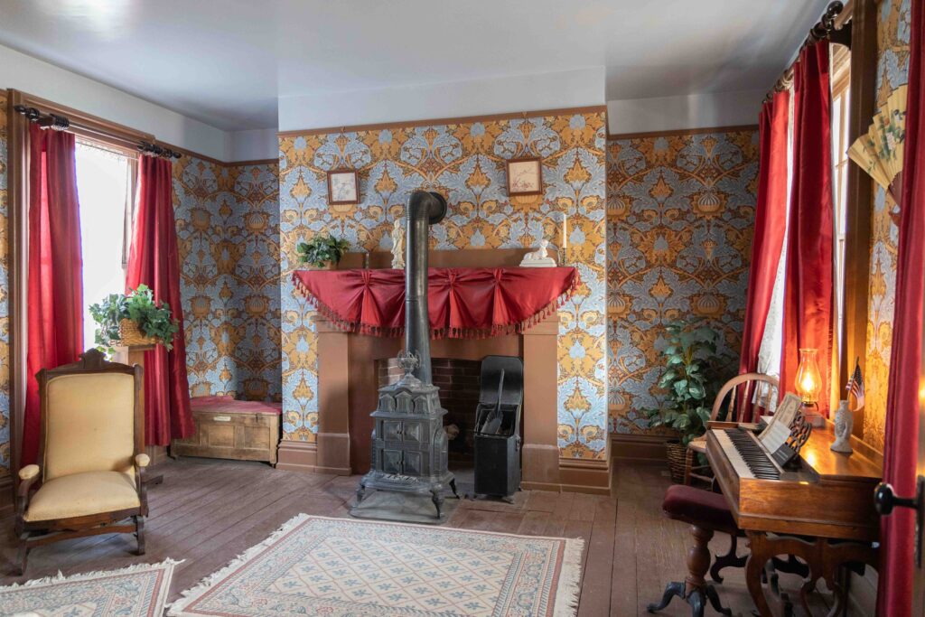 Small parlor in the Officers' Quarters with a couple of chairs, wood stove/fireplace, and throw rugs