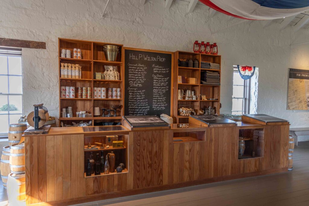 Replica of a post trader's store. Goods on shelves behind the counter and a chalkboard with list of items available.