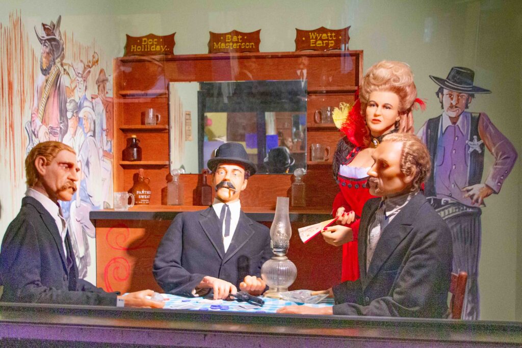 Mannequins dressed as Doc Holliday, Bat Masterson, and Wyatt Earp at a poker table with a woman and sheriff standing nearby