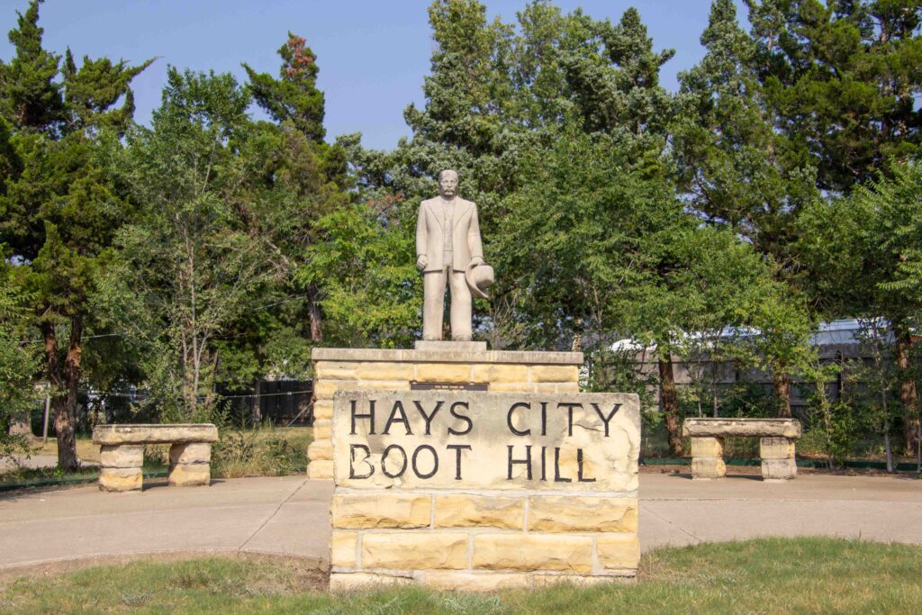 Stone marker that says "Hays City Boot Hill" and a statue of a man holding a hat atop another stone stucture.