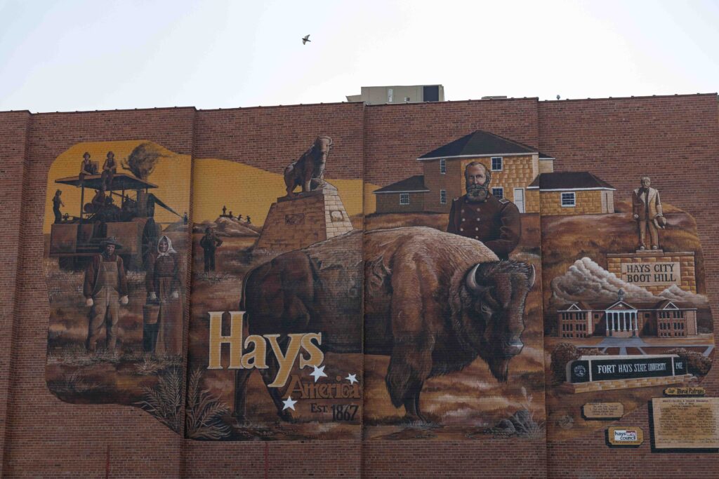 Mural on a brick building. A bison is in the foreground. The mural also depicts historic landmarks and people of Hays.