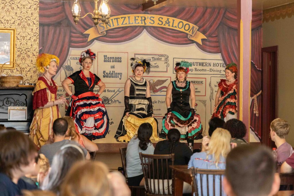 Five women dressed as 1800s saloon showgirls on a stage
